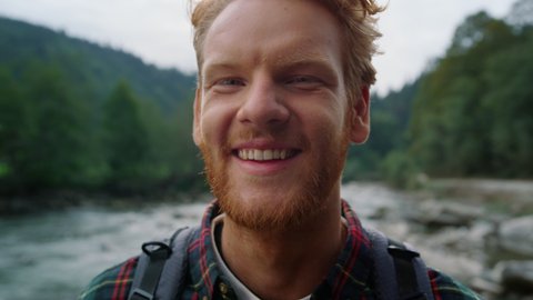 Smiling hiker standing in mountain landscape. Portrait of redhead man looking at camera outdoor. Closeup laughing guy posing at camera. Male happy face emotion