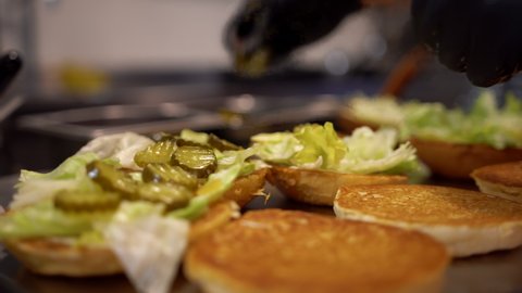 Preparing burgers in a fast food restaurant. Close up view of a fast food worker adding vegetables to the burger