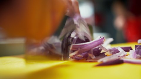 Close up view of a knife cutting red onion into thin slices. Close up view of a cook quickly chopping a purple vegetable