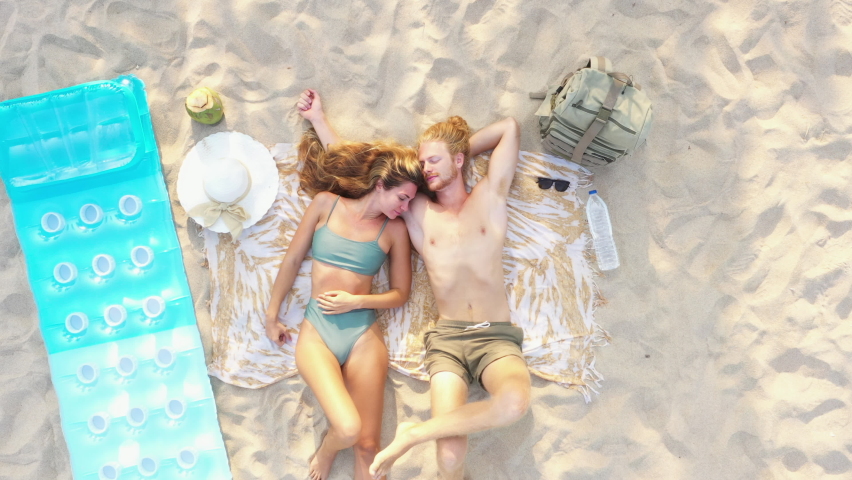 Top view of happy romantic sweet young caucasian couple relaxing by laying down and sleeping on the beach near the sea, They spending time together during summer vacation or honeymoon trip.