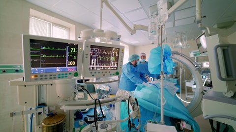 Hospital monitor in the operating room. Screen shows vital signs of a patient on the background of surgical procedure. Teamwork of doctors.