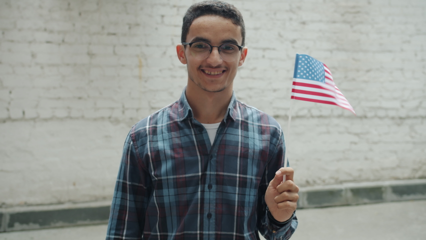 Slow motion of happy Arab man holding American national flag and smiling outdoors against urban background. People and world countries concept.