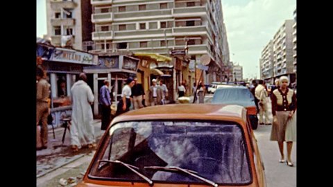 Alexandria, EGYPT, AFRICA - circa 1981: Egyptian people in local bazaar in traditional Arab dress and mosque minaret in Alexandria city. Vintage cars in traffic. Historical archival of Egypt in 1980s.