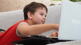 boy using a laptop for playing online games and wearing headphone at home, a boy at a computer or tablet at home on the couch, communicating with friends, blogging, studying online