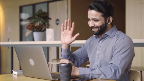 Happy indian business man customer support agent or salesman wearing headset talking, having virtual meeting working on laptop computer giving online training, remote class on video conference call.