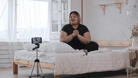 A confident overweight woman feminist sitting on bed and talking about her experience about feminism and body positivity on video