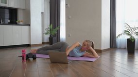 Strong young woman in activewear lying on yoga mat, training legs and watching video on portable laptop. Concept of people, sport and technology.