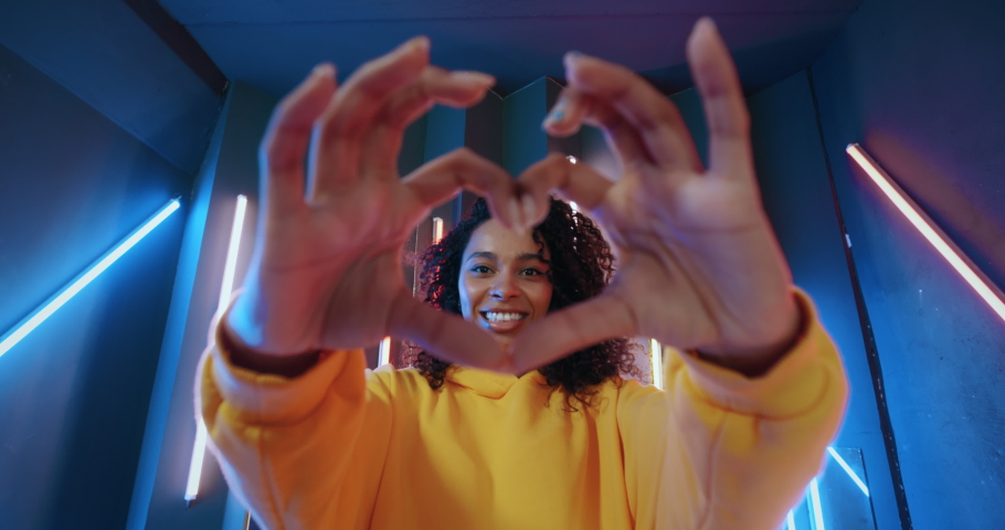 Wide angle positive african american black woman in yellow hoodie dancing in night club backlit with colorful neon stripes lights. Gen z happy urban female doing modern expressive dance with her hands Royalty-Free Stock Footage #1071100336
