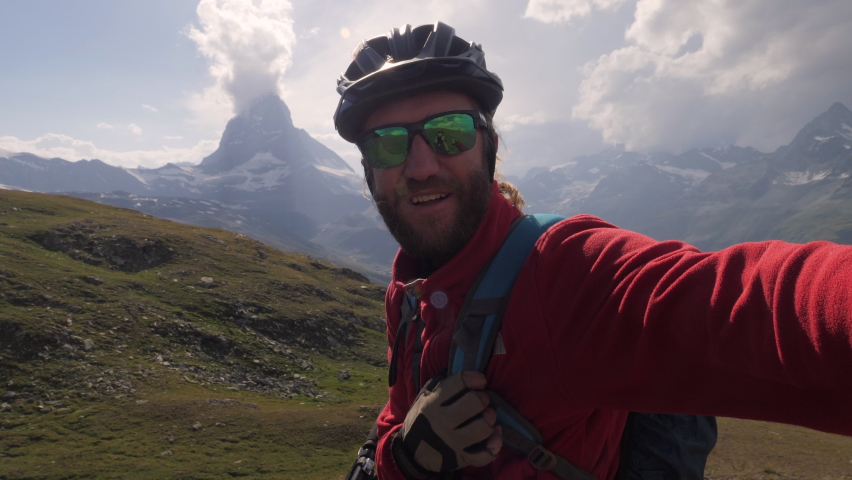 Young adult mountain biker taking selfies on trail with his bike. Man mountain biking in Zermatt, Switzerland, takes cool selfie with Matterhorn peak in the background.