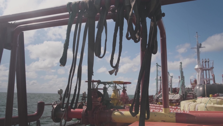black ropes waved by wind hang on oil tanker deck against endless sea under blue sky with clouds at bright sunlight closeup