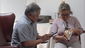 Asian elderly family relaxing together at home. Senior couple using smartphone reading e-book or social media. Retirement family husband and wife enjoy home leisure activity lifestyle with happiness