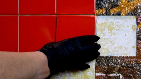 Worker hands placing small red ceramic tile on wall during repair kitchen or bathroom. Loft interior with your own hands at home. Close-up.