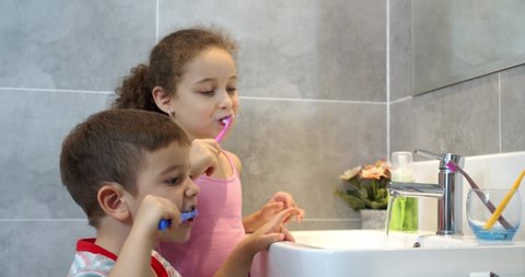 Portrait happy cute young children brushing teeth in bathroom and smiling. Children daily healthcare routine. Caucasian kids brushing looking at mirror at home. Lifestyle.