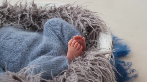 Newborn baby boy wearing knitted blue costume wakes up and hiccups. Sleepy infant looking at camera
