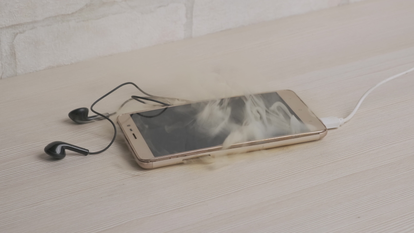 Fire phone battery while charging on desk at home or in office closeup, smartphone smokes, starting to burn. Royalty-Free Stock Footage #1071137092