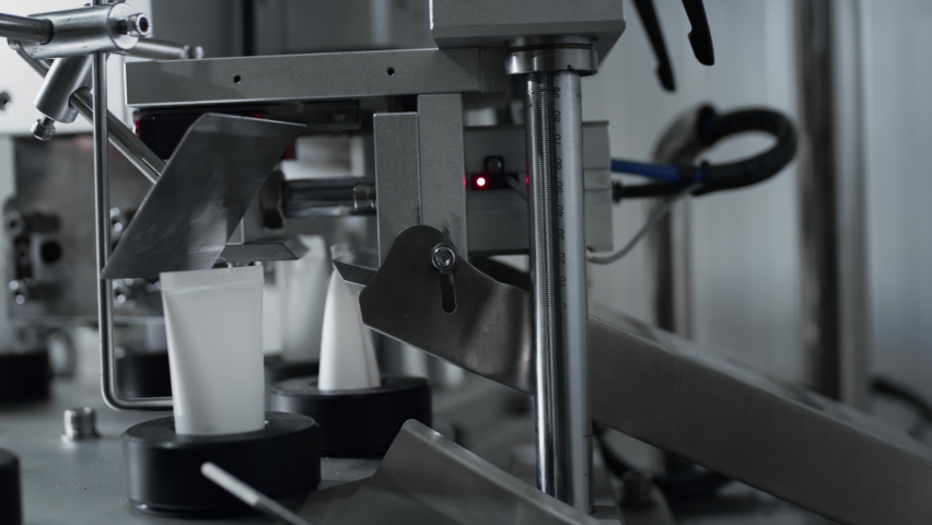 Automatic machine in the factory for making cream. Cosmetic or pharmaceutical production. The mechanism creates a packaging for the cream, a tube, phial or a bottle made of plastic. Royalty-Free Stock Footage #1071140122