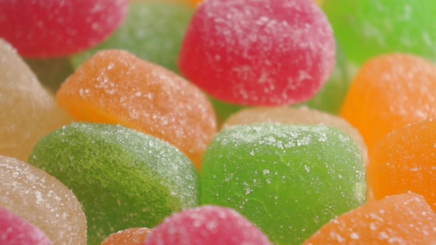 Hand takes colourful piece of jelly marmalade from dish close up
