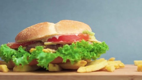 Golden fries and a burger fall from top to bottom on a wooden board. Slow motion. Flying food. Fast food. Blue background.