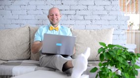 Crazy, cheerful, elegant man in shirt and bow tie fooling around and looking through binoculars made from his own hands on virtual date via call. Happy man talking on video chat in self-isolation.
