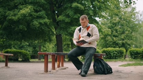 A funny nerdy man is reading book outdoor. A bookworm loser with glasses is preparing to exam.