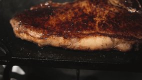 This slow motion video shows a close up view of a juicy steak sizzling and being flipped over the edge of a flat top cooking area.