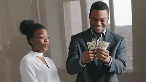 Excited Ethnic African American man made good deal, woman got big fat payoff contract. Gets lot money dollars out of envelope, shows girl friend, young people feel happy emotionally laughing celebrate