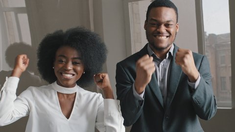 Excited ethnic African American office workers rejoicing win shouting yes, man woman waving clapping hands. Employees received offer contract, business partners satisfied work result celebrate success