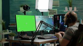 Gamer streaming online videogames on professional powerful computer with green screen, mock up, chroma key display. Streamer playing space shooter game at isolated desktop holding wireles controller