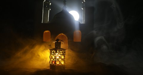 Ornamental Arabic lantern with burning candle glowing at night. Realistic mosque miniature on background. Festive greeting card, invitation for Muslim holy month Ramadan Kareem. Selective focus