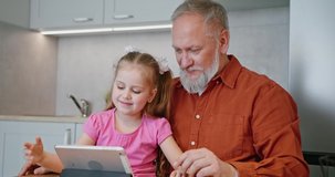Grandpa and cute small kid daughter bloggers recording lifestyle vlog on digital tablet talking looking at phone using funny application having fun with tech education concept sit at home table