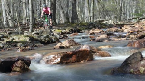 Cinemagraph of out of focus man biking along a river. Unrecognizable young man riding a mountain bike beside splashing cold stream water.