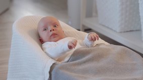 Newborn baby boy lying on white baby bouncer 1.5 month old caucasian infant covered with a gray blanket in rocking chair at home. High quality 4k footage