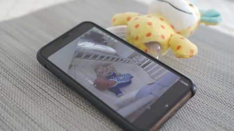 SAINT PETERSBURG, RUSSIA - CIRCA APRIL, 2021: Video baby monitor app on phone, on smartphone screen newborn infant sleeping in crib. High quality 4k footage