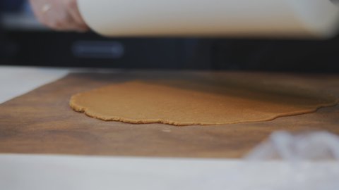 the hands of a Caucasian pastry chef roll the dough with a white rolling pin. The baker rolls out the dark dough for the cake layer. Places a round punch and cuts off the cake. Close-up