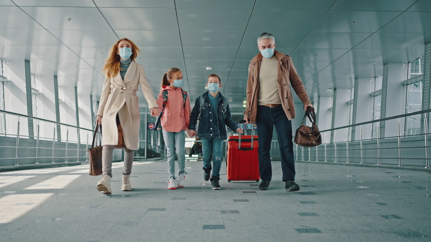 Family vacation. Mother and father holding hands of their children and walking down the airport corridor to flight, everyone wearing protective medical masks, slow motion Royalty-Free Stock Footage #1071165799
