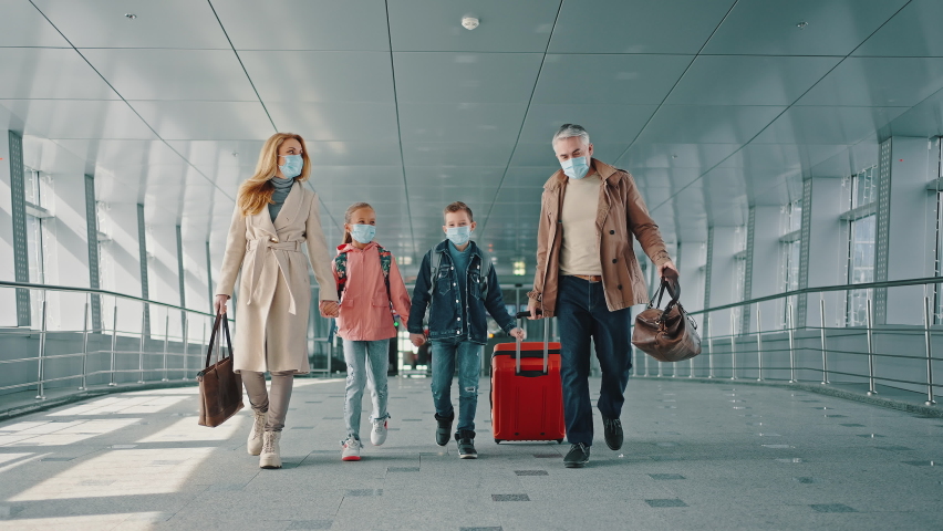 Family vacation. Mother and father holding hands of their children and walking down the airport corridor to flight, everyone wearing protective medical masks, slow motion | Shutterstock HD Video #1071165799