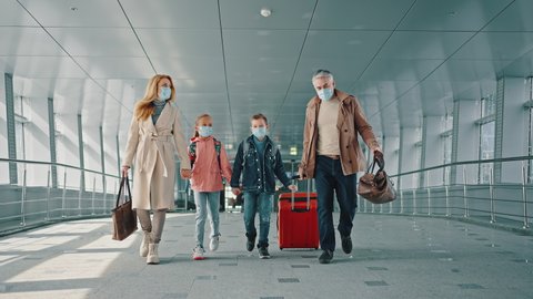 Family vacation. Mother and father holding hands of their children and walking down the airport corridor to flight, everyone wearing protective medical masks, slow motion