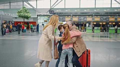 Family reunion. Happy children with mother meeting dad from business trip at airport, embracing and laughing, side view, slow motion