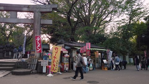 tokyo, japan - october 20 2019: Pan video of tourists sightseeing a retro store called Toshogu Daiichi Shop beside the stone torii gate of Ueno Tosho-gu shrine classed as Important cultural property.