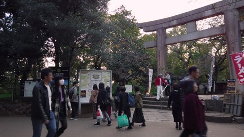 tokyo, japan - october 20 2019: Pan video of tourists visiting the Ueno Tosho-gu shrine classed as Important cultural property passing below his stone torii gate beside the retro Toshogu Daiichi Shop.