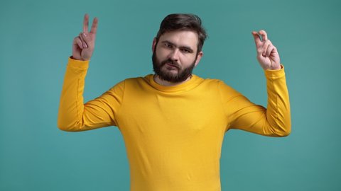 Handsome man showing with hands and two fingers air quotes gesture, bend fingers isolated on blue background. Guy in yellow wear. Not funny, irony and sarcasm concept.