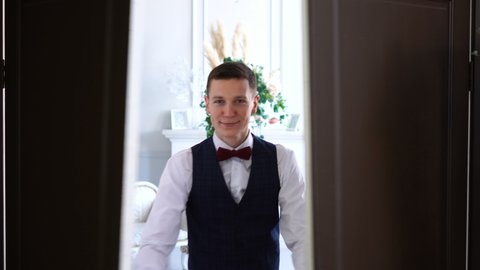 Handsome young man possibly groom opens double wooden door and smiles at camera
