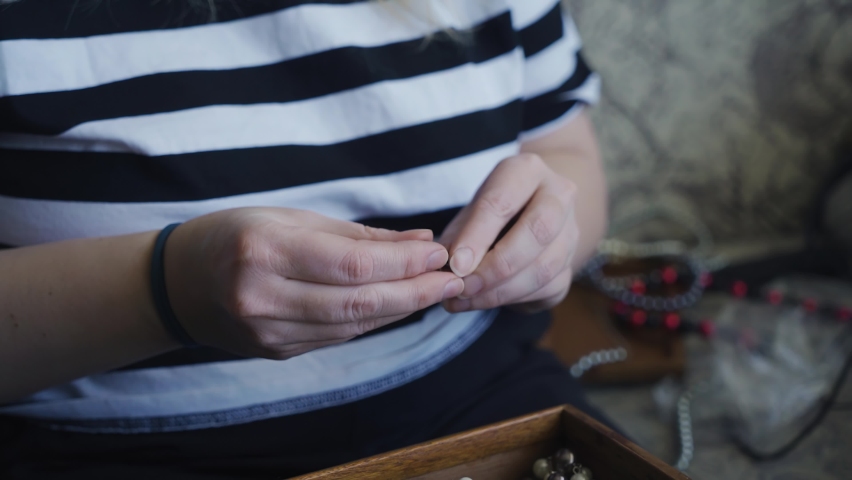 The girl takes out jewelry from a wooden box and examines them. She touches and turns them in her hands.