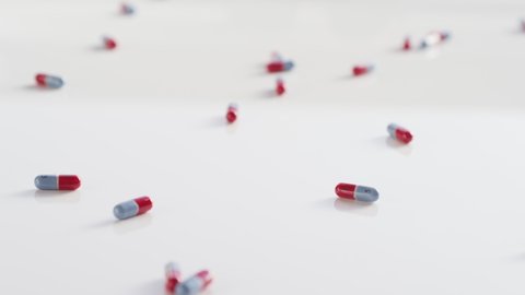 Red and blue pills drop and tumble on a white surface in slow motion