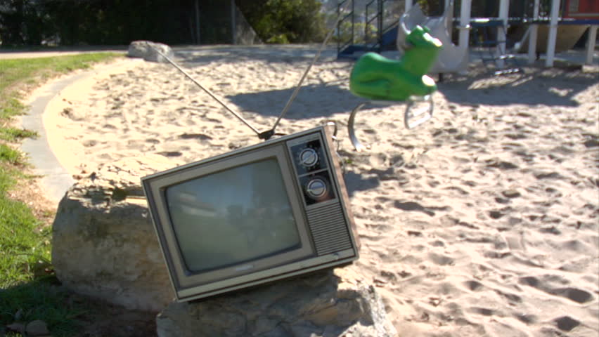 retro tv on a playground.  In the background is a frog ride. 