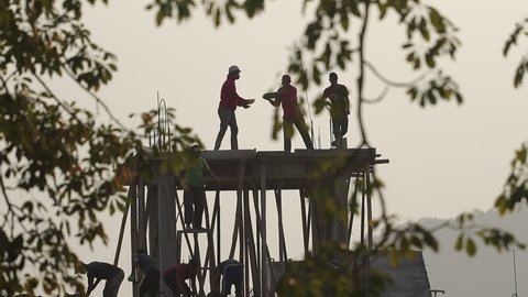 Pokhara, Nepal - November 20 2020: Silhouetted construction workers working on a site during evening hour.  Workers carrying and pouring concrete for constructing house ina traditional way in Nepal.