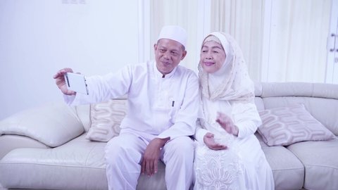 Muslim senior couple taking selfie picture by using a cellphone while celebrating Eid Mubarak in the living room. Shot in 4k resolution