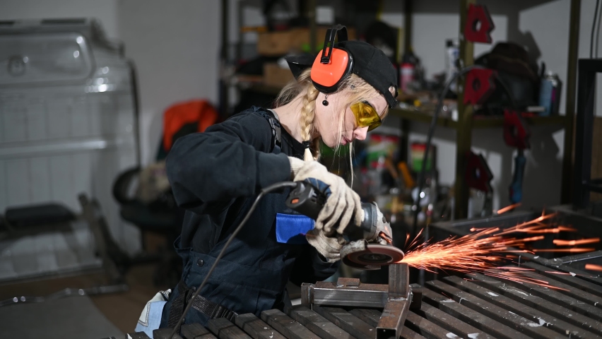 Video of a caucasian girl blonde worker in protective equipment working with an angle grinder at a factory | Shutterstock HD Video #1071184006