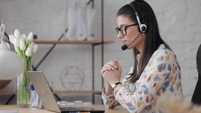 Young caucasian business woman in glasses wearing headphones communicating by video call. Female speaking looking at laptop computer, online conference distance office chat, virtual training concept.