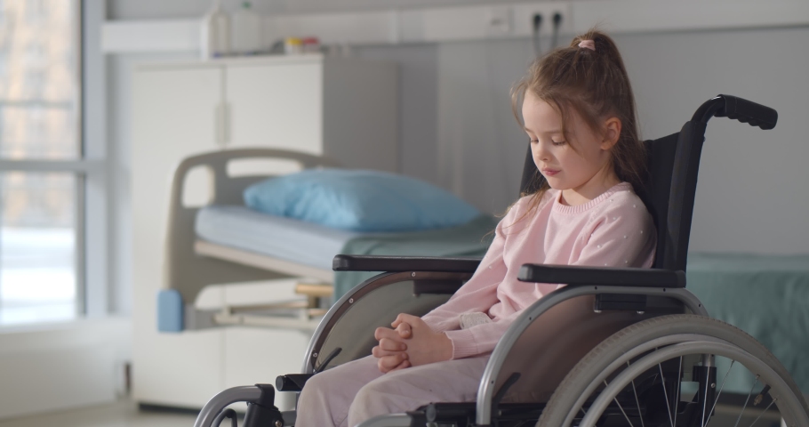Sad little girl in a wheelchair in hospital ward looking at camera. Portrait of upset and lonely disables child patient sitting in wheelchair at pediatrics department Royalty-Free Stock Footage #1071189250